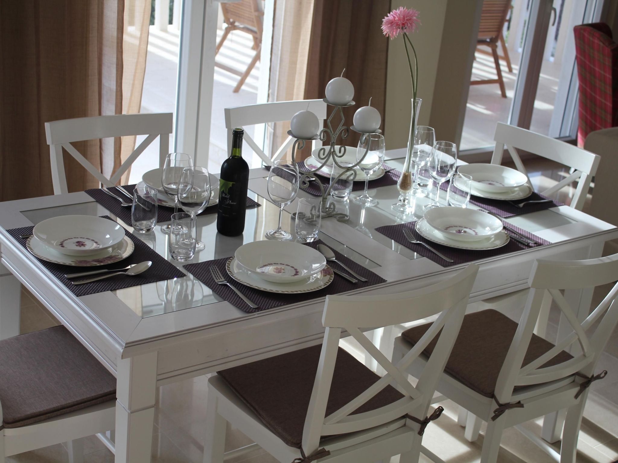 A dining table set with white plates, clear glasses, and a bottle of wine.