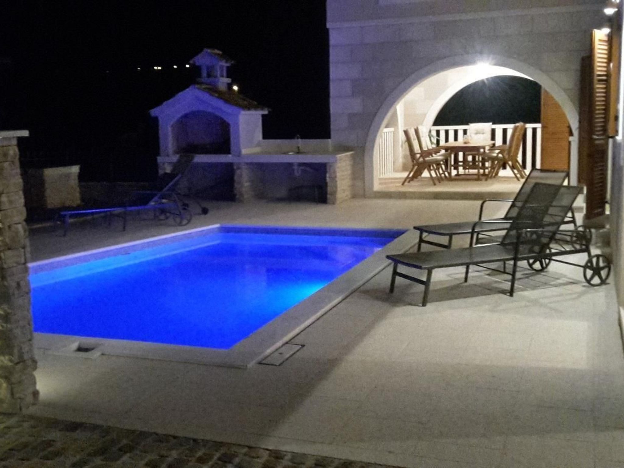 A swimming pool with a blue light, outdoor seating area, and a stone building structure in the background.