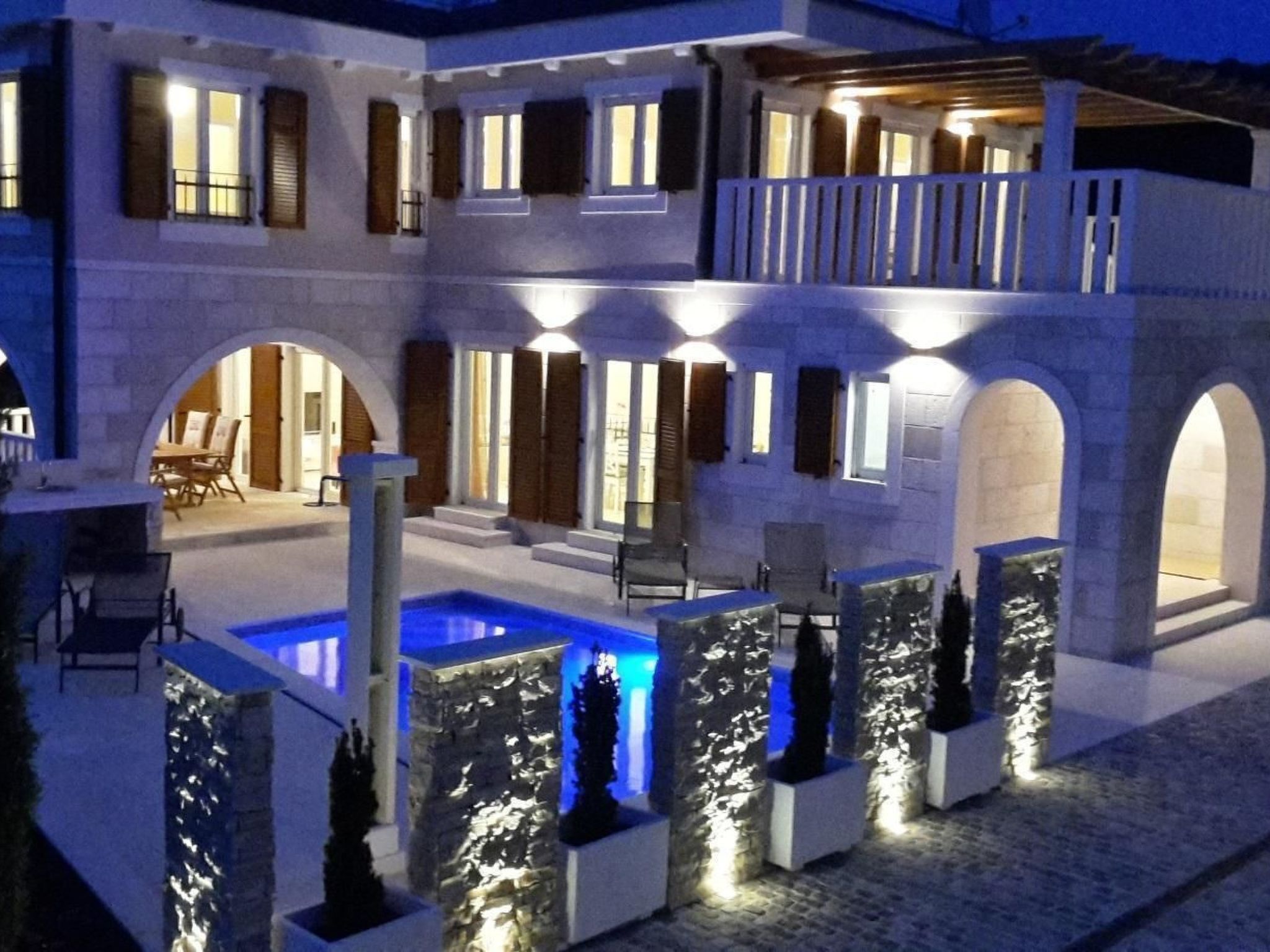 Un bâtiment à deux étages doté d’une piscine, d’un espace extérieur aménagé et de piliers en pierre.
