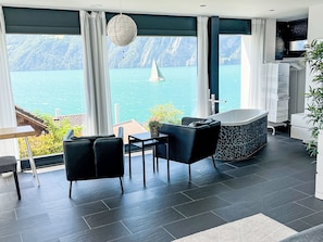A modern room with a view of a lake, a bathtub, and a dining area. - Villa am See 3 - Beach House by Interhome (Sisikon)