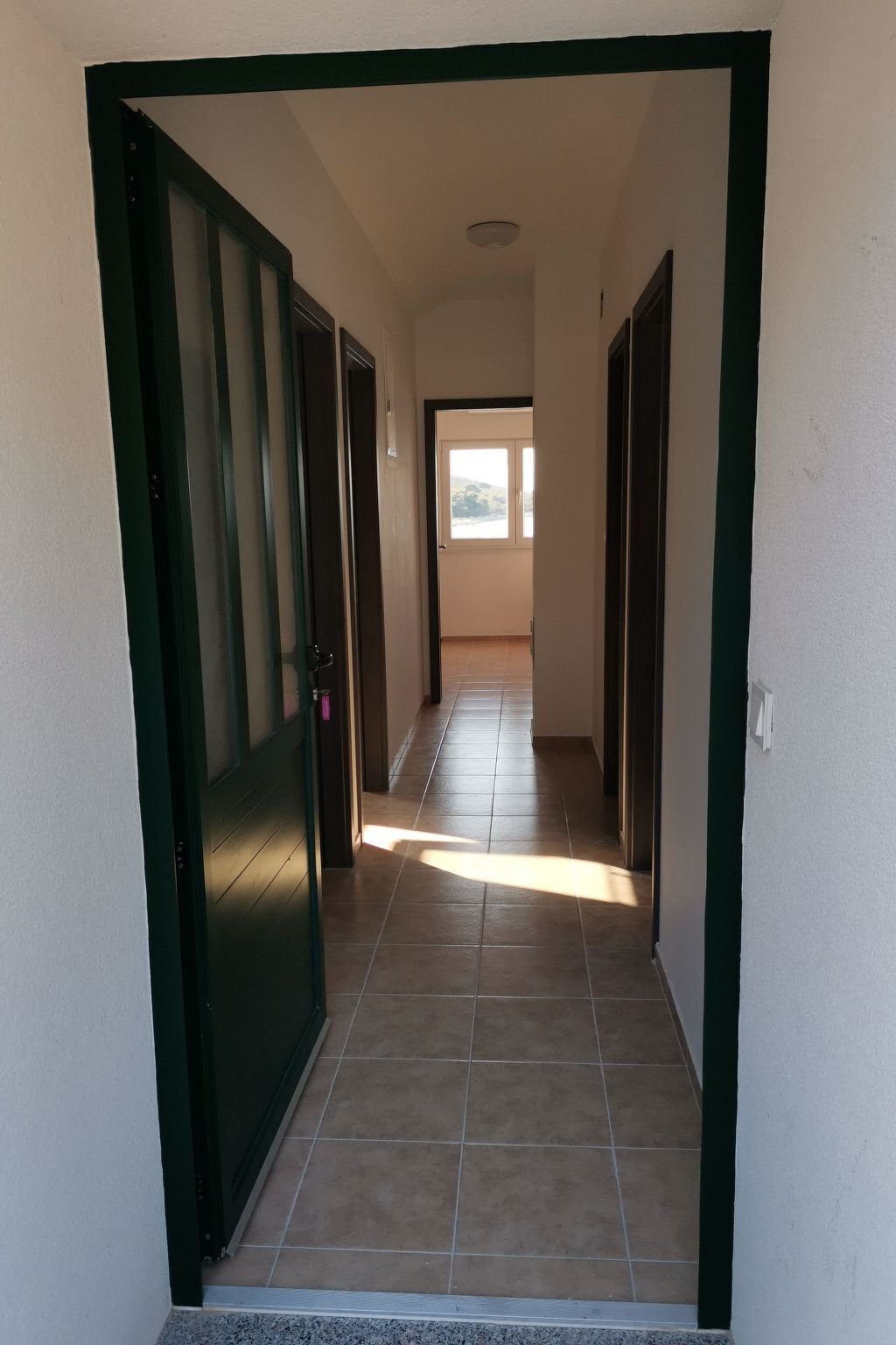 A hallway with a tiled floor leading to a room with a window.