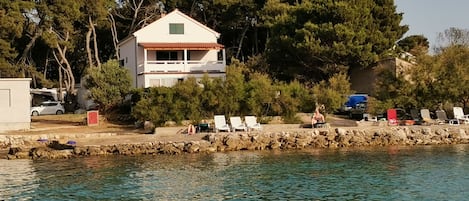 A coastal property with a white building, a stone wall, and a row of beach chairs.