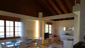 Amplia sala de estar con una mesa de comedor, sillas y televisor. Se observa una cocina con mostrador y alacenas.