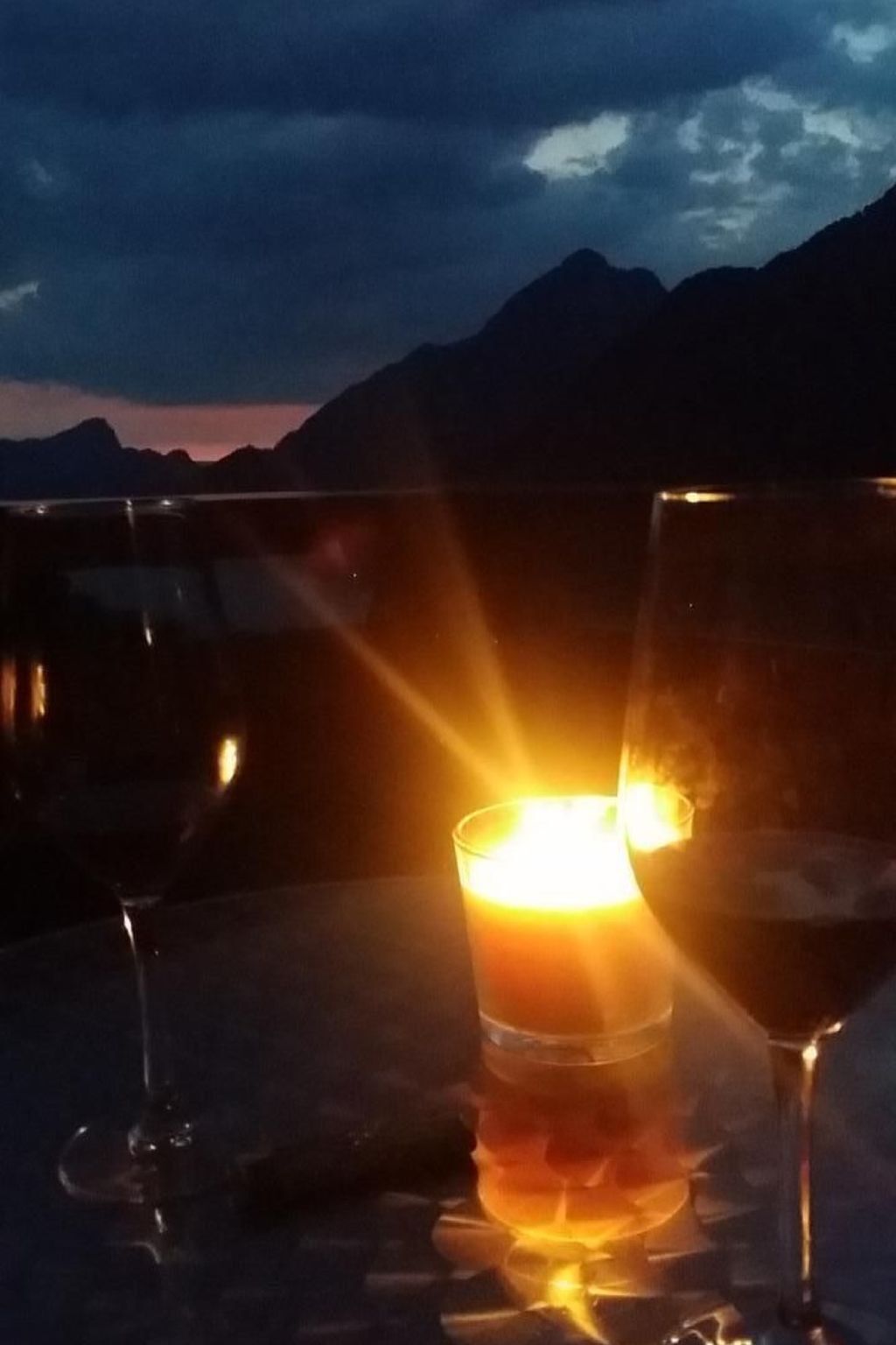 Ein Tisch mit zwei Weingläsern und einer Kerze, vor einer Bergkulisse.