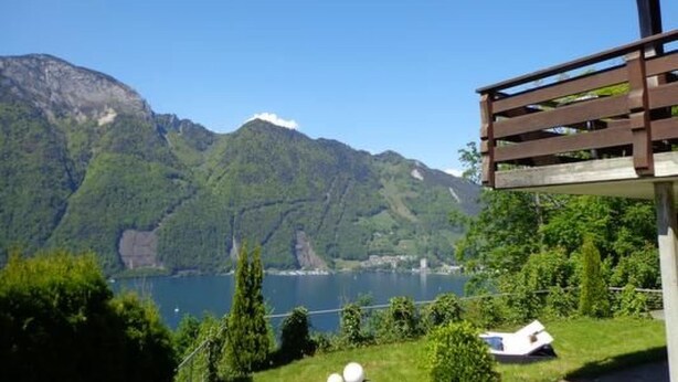 Vista de la montaña con un lago, una terraza de madera y un pequeño bote.