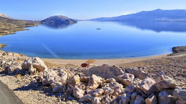 A rocky shoreline with a clear blue lake and a small island in the distance. - für 6 Personen ca. 65 m² in Zubovici, Adriaküste Kroatien (Kroatische Inse by Interhome (Pag/Zubovići)