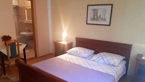 A bedroom with a wooden bed, a bedside table, a nightstand, a chair, a desk, and a bathroom with a sink and mirror. - für 6 Personen ca. 65 m² in Zubovici, Adriaküste Kroatien (Kroatische Inse by Interhome (Pag/Zubovići)