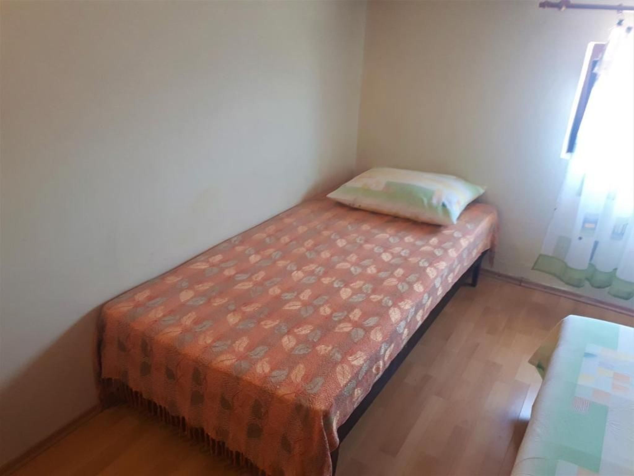 Une petite chambre avec un lit simple, une couvre-lit à motifs, un oreiller et une fenêtre avec des rideaux.