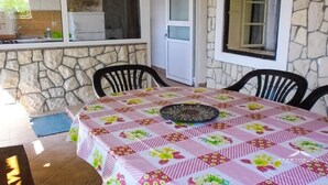 A dining area with a table covered by a floral tablecloth, stone walls, and a window with a view of the kitchen. - für 4 Personen  + 2 Kinder ca. 60 m² in Zubovici, Adriaküste Kroatien (Kro by Interhome (Pag/Zubovići)