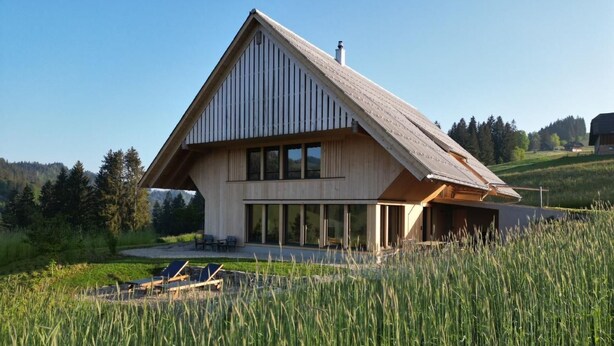 A modern house with a sloped roof, large windows, and a view of a grassy field.