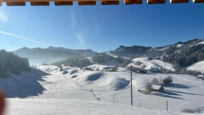 A snow-covered landscape with a clear sky, a wooden structure in the foreground, and distant mountains.