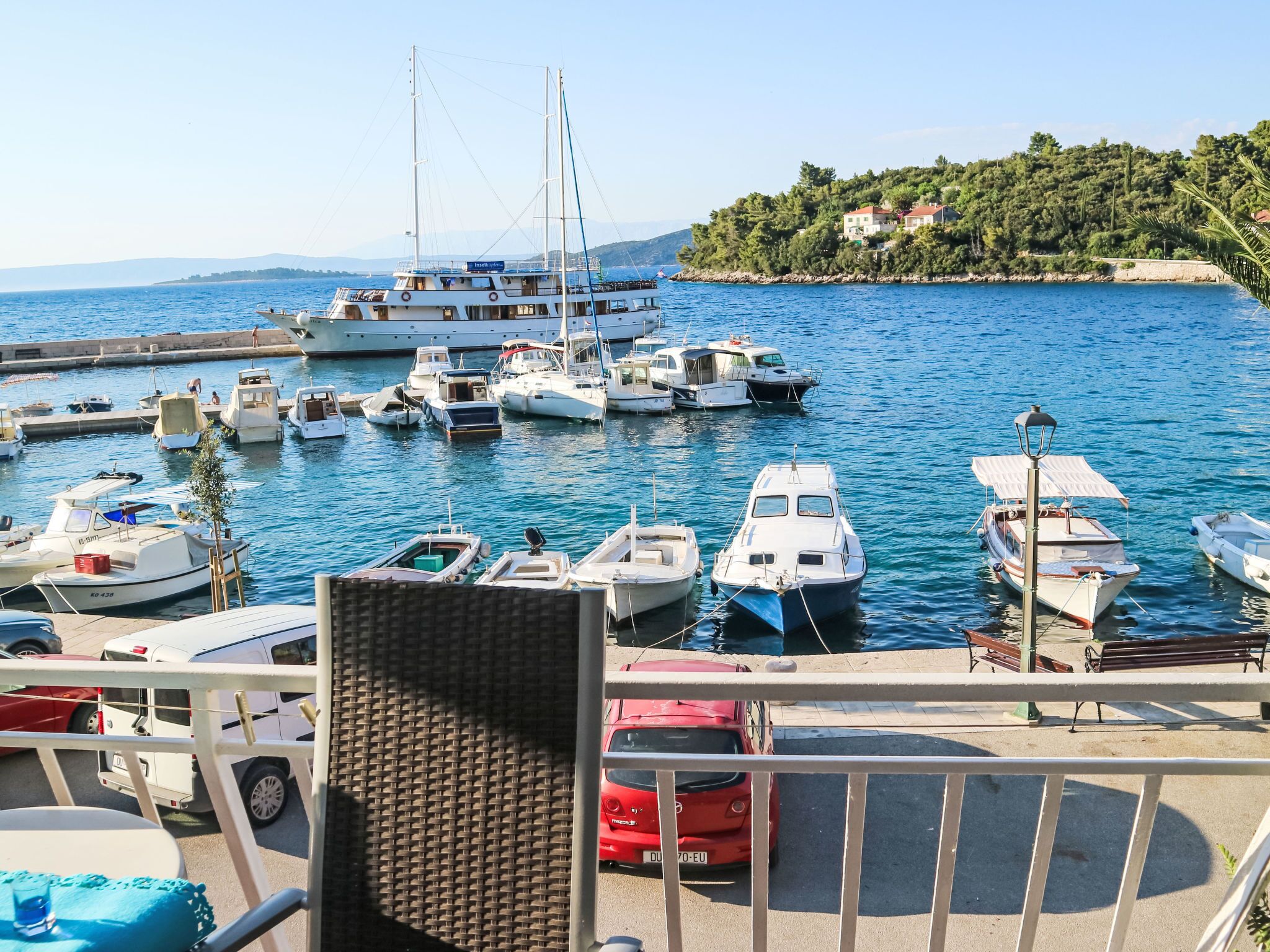 A marina with various boats docked, a clear view of the water, and a hillside with buildings in the background.