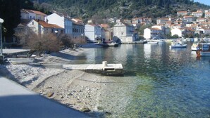 Un pueblo costero con edificios a lo largo del paseo marítimo, un río claro y un paisaje montañoso de fondo.