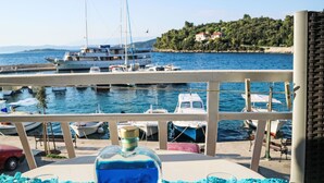 Una mesa con una botella y dos vasos, con vistas a un puerto deportivo con barcos y una costa lejana.