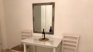 Ein kleiner, weißer Esstisch mit zwei Stühlen, einer Weinflasche und einem Spiegel an der Wand.