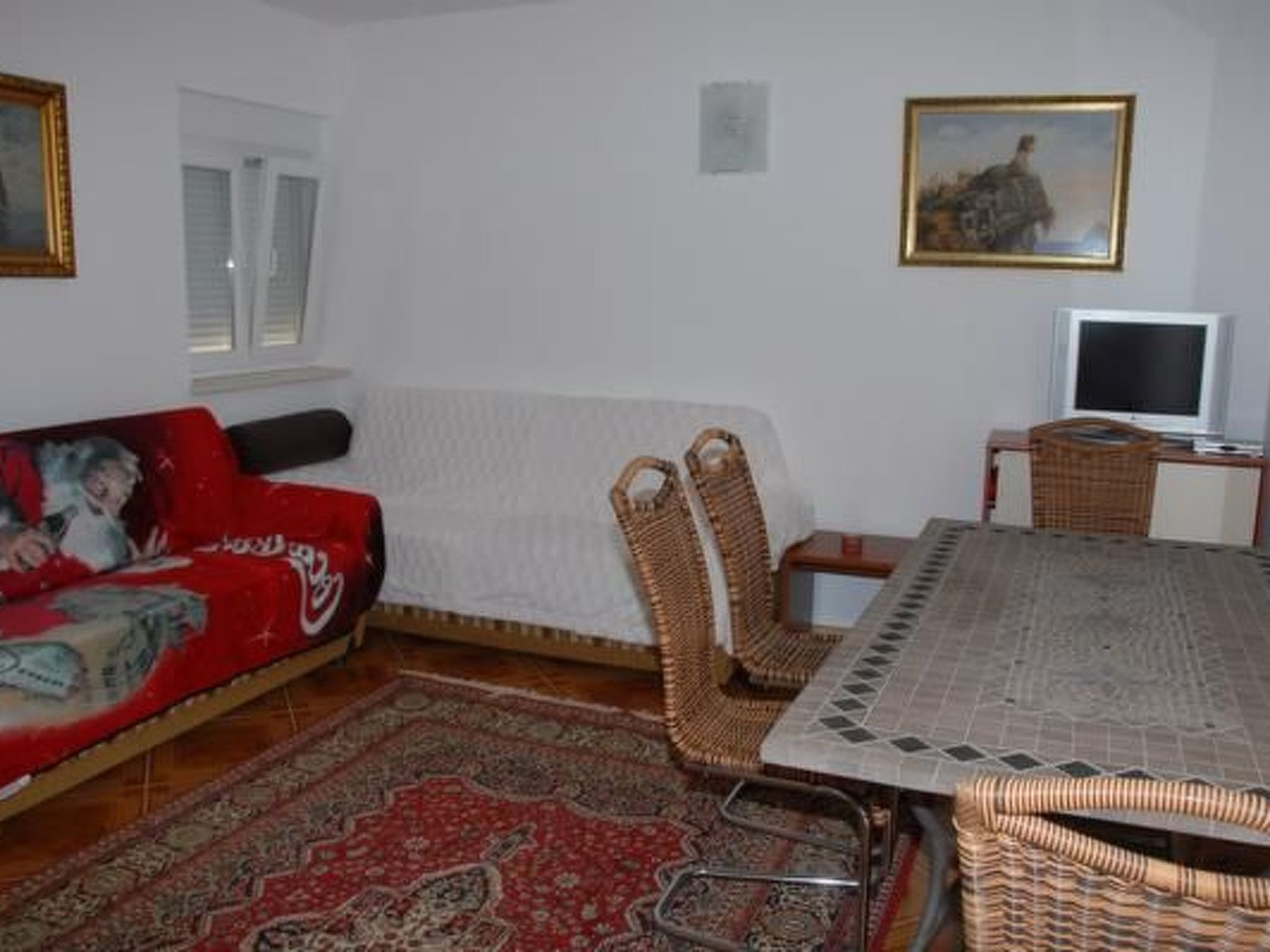Ein Wohnzimmer mit einem roten Sofa, einem weißen Sessel, einem Esstisch und einem Fernseher.