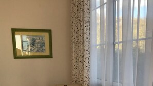 Ruokailutila, jossa on pyöreä pöytä ja neljä beigenväristä tuolia, viinipullo, seinällä oleva kehystetty kuva ja ikkuna, jossa on läpikuultavat verhot.
