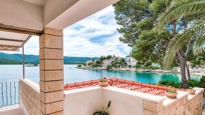 Ein Balkon mit Terrakottafliesen, Blumentöpfen und Blick auf einen See mit Gebäuden im Hintergrund.