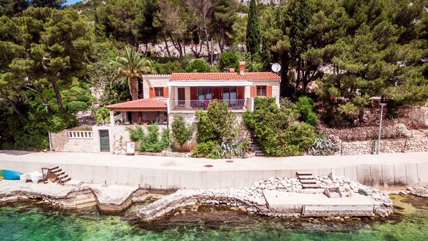 Ein Küstenhaus mit Balkon, einer Steinmauer und freiem Blick auf das Meer.