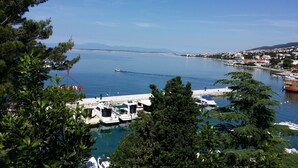 Un puerto deportivo con barcos amarrados, rodeado de vegetación y una vista despejada de un horizonte urbano lejano.