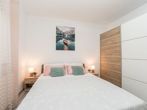 Ein Schlafzimmer mit einem Bett, zwei Nachttischen mit Lampen, einem Holzschrank und einem Gemälde einer Berglandschaft.