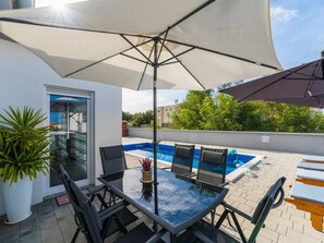 Eine Terrasse im Freien mit einem Glastisch, Stühlen und einem Pool.