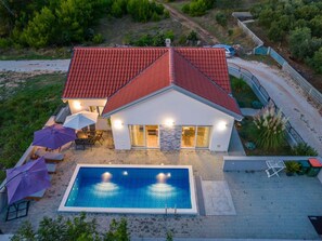 Ein zweistöckiges Haus mit Swimmingpool, einer Terrasse und Gartenmöbeln sowie einem roten Ziegeldach.