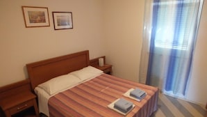 Una habitación de hotel con una cama de madera, ropa de cama a rayas, dos mesitas de noche y una ventana con cortinas.