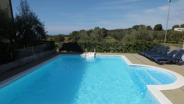 Una piscina rectangular con superficie de agua azul cristalina, rodeada por un muro bajo y una fila de tumbonas a un lado.