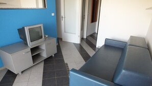Una habitación con un sofá azul, un televisor pequeño sobre un mueble, y una puerta que da a otra habitación.