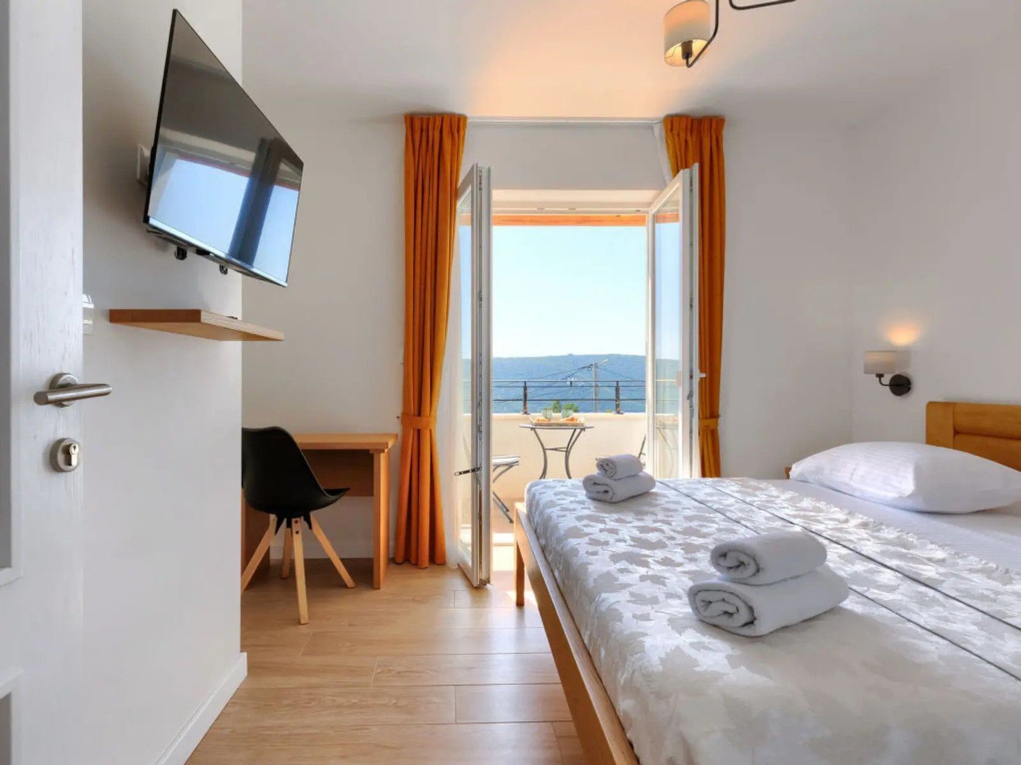 A hotel room with a bed, a desk, a chair, a TV, and a balcony with a view.