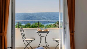Ein Balkon mit zwei Stühlen und einem kleinen Tisch, mit Blick auf eine schöne Landschaft aus Hügeln und einem Gewässer.