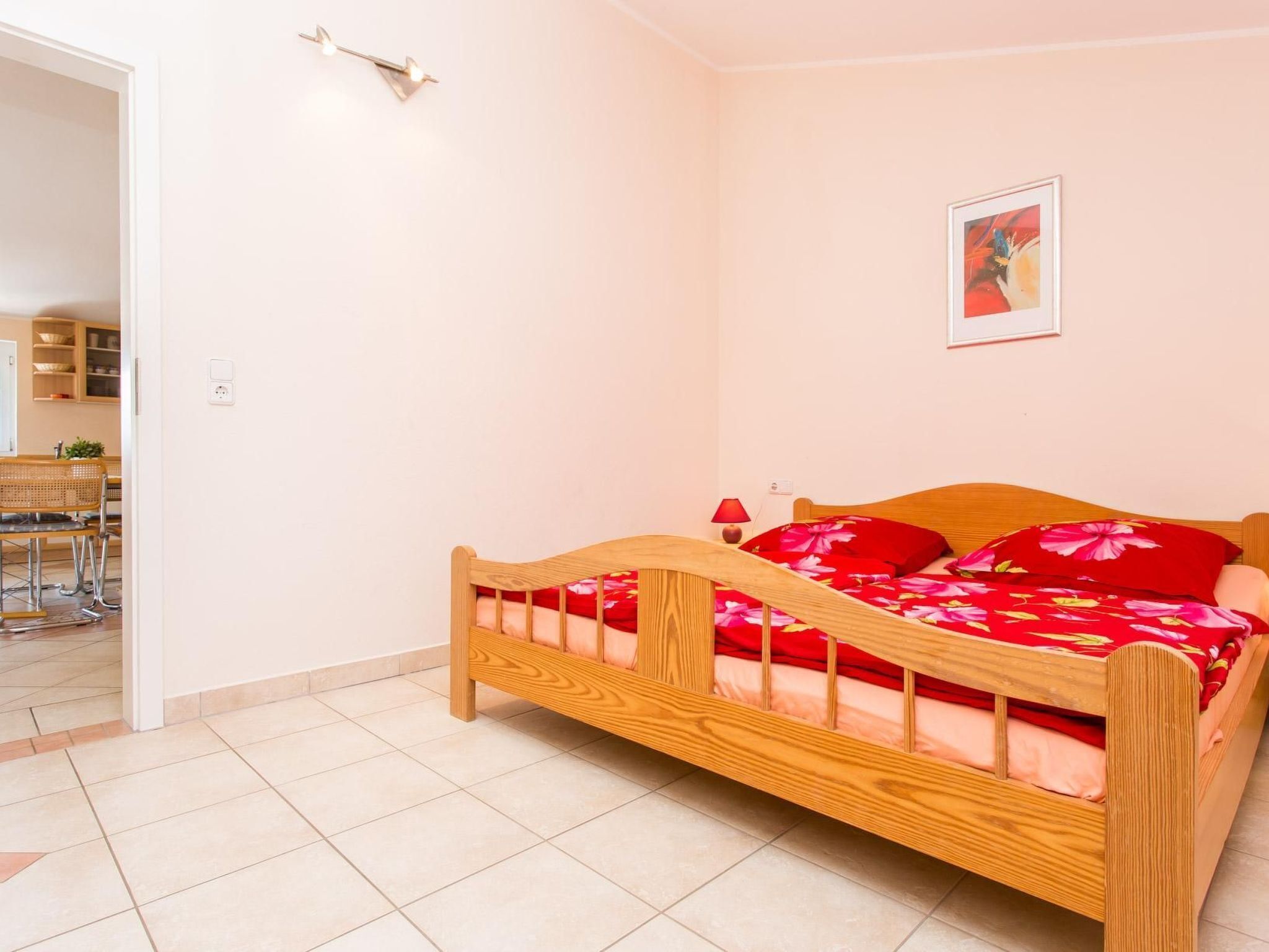 A bedroom with a wooden bed, a red floral bedspread, and a small bedside table with a lamp.