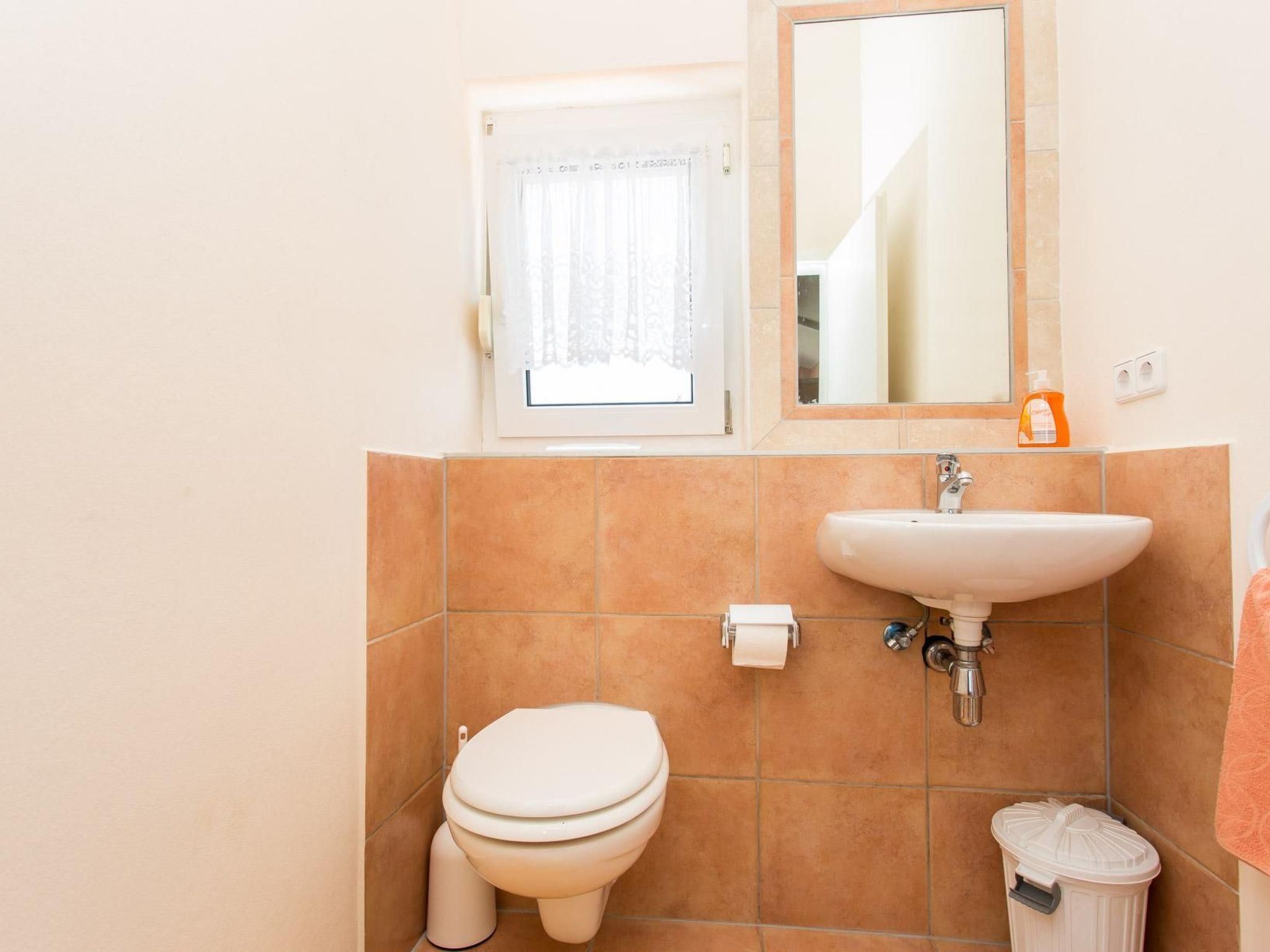 A bathroom with a toilet, sink, and a trash bin.