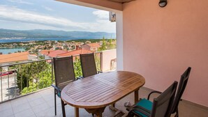 Un balcón con mesa y sillas de madera, con vistas a un pueblo costero y montañas.