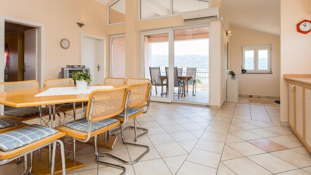 Un comedor con una mesa y sillas, un reloj en la pared y vista al mar a través de puertas de vidrio.