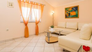 Un salón con un sofá beige, una mesa de centro de vidrio y cortinas naranjas.