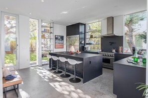 A modern kitchen with a central island, bar stools, and a large window. - Luxe 9BDR Retreat w/ Putting Green + Game Room | Bouldin Collective by AvantStay (Austin)
