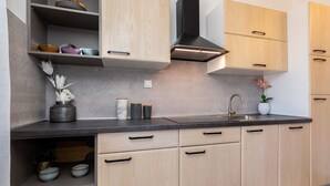 A modern kitchen with light wood cabinets, a black range hood, and a granite countertop. - Pension Tina Appartement 2 by Interhome (Krk/Šilo)