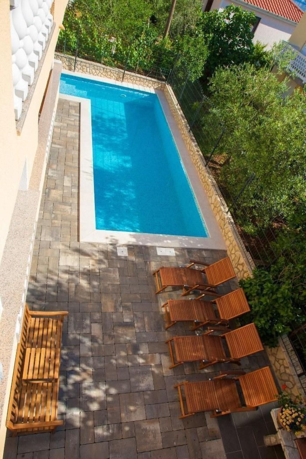 A rectangular swimming pool with a tiled deck and wooden lounge chairs.