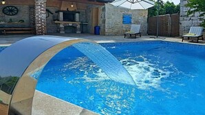 A swimming pool with a waterfall feature, surrounded by stone walls and outdoor furniture. - Vacation home Simone by Interhome (Dracevac)