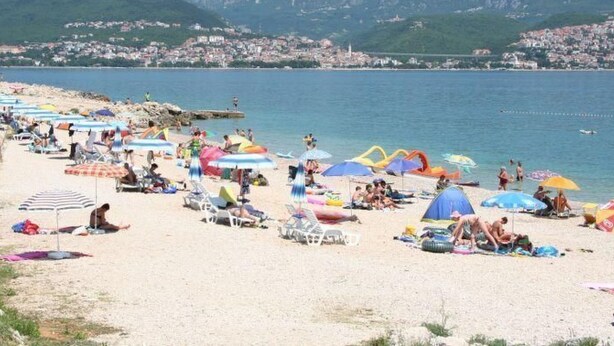 A beach with rows of sunbeds and umbrellas, a clear view of the sea, and a town in the background. - Svoboda 2 by Interhome (Krk/Šilo)