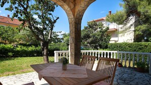 An outdoor patio with a table and chairs, surrounded by stone flooring and greenery. - Svoboda 2 by Interhome (Krk/Šilo)