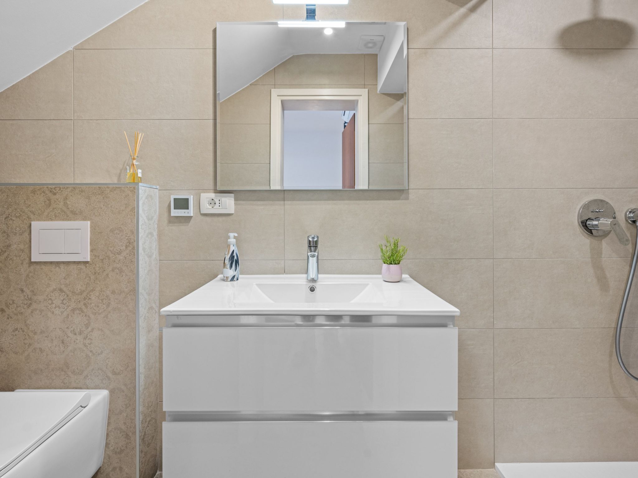 A modern bathroom with a white vanity, a mirror, a small plant, and a shower.