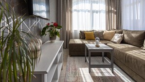En moderne stue med sofa, sofabord, fjernsyn ophængt på væggen og en potteplante.