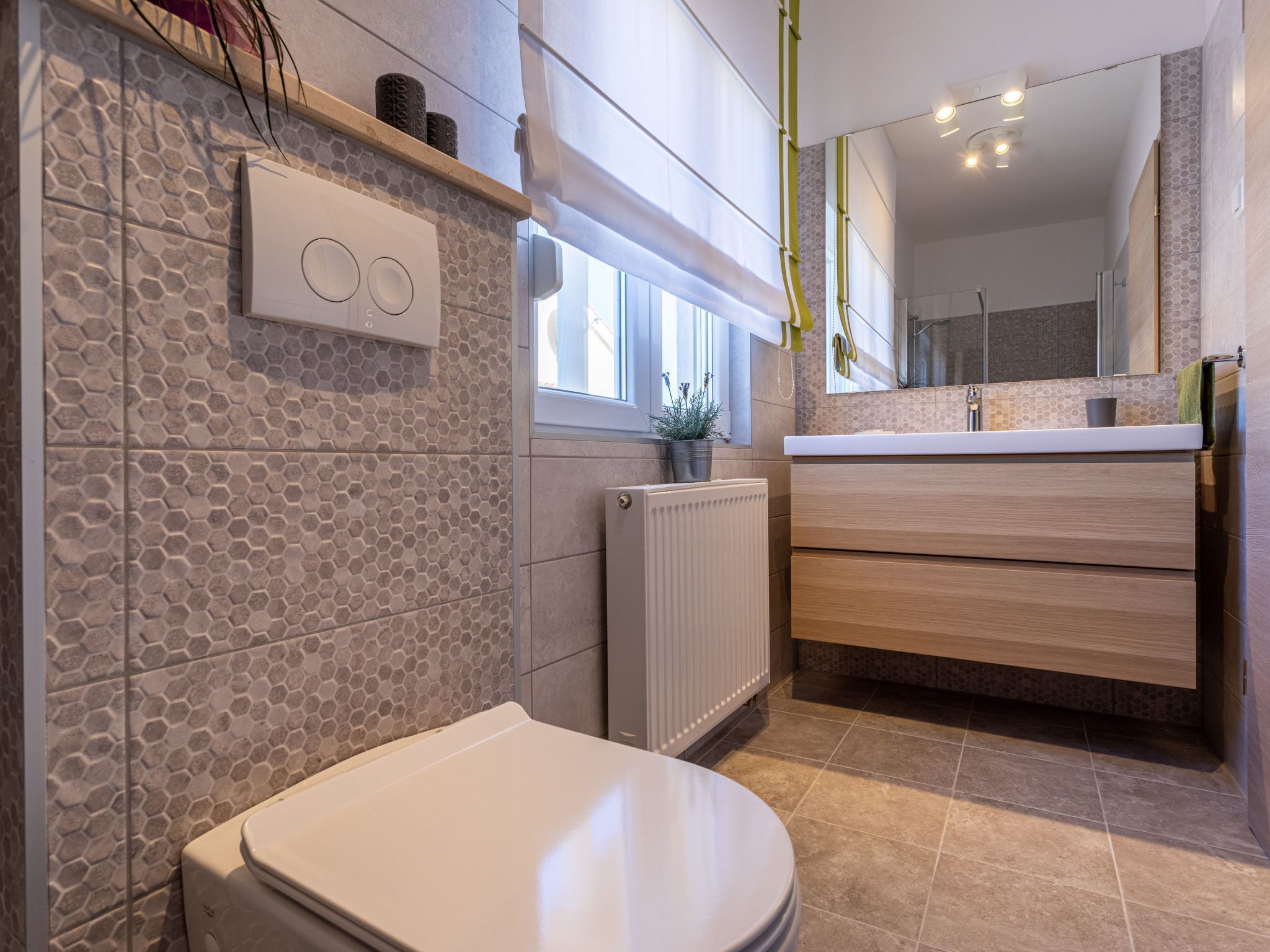 Ein modernes Badezimmer mit Toilette, Heizkörper, Waschbecken mit Spiegel und Fenster.