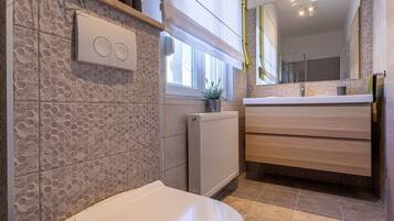 Ein modernes Badezimmer mit Toilette, Heizkörper, Waschbecken mit Spiegel und Fenster.