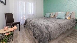 A bedroom with a bed, a chair, a small table with flowers, and a window with curtains. - Moderne Wohnung Grzetic by Interhome (Krk/Šilo)