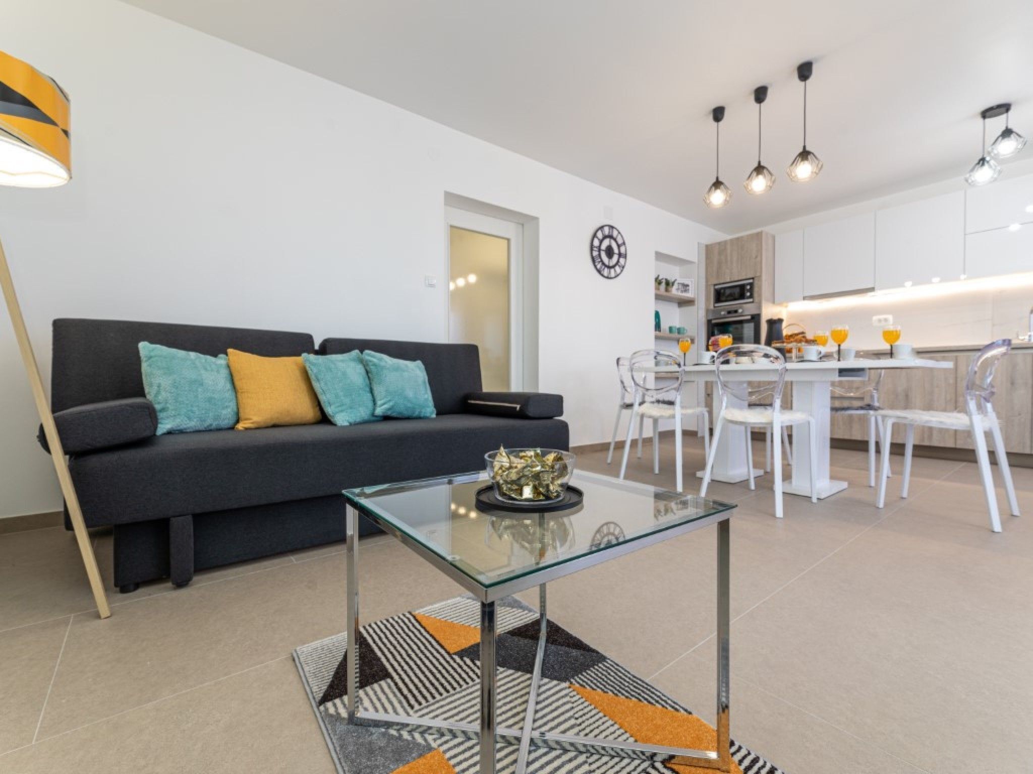 A modern living room with a dark sofa, a glass coffee table, and a dining area with a white table and chairs.