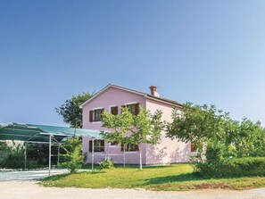 A pink two-story house with a green roof, surrounded by greenery and a clear sky. - Vacation home Korina by Interhome (Cere)